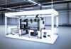 3D Printing Industry Year in Review: December 2023 High-resolution realistic photograph of a 3D printer in an industrial setting, showing a large-format part being printed, with branding from companies like BCN3D or ADDMAN. Avoid futuristic or stylized elements.