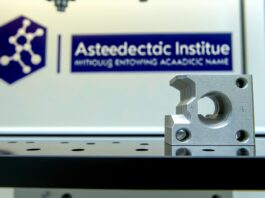 High-resolution realistic photograph of a 3D printed aluminum part enhanced with nanoparticles, placed on a lab bench with MIT branding in the background. Avoid futuristic or stylized elements.